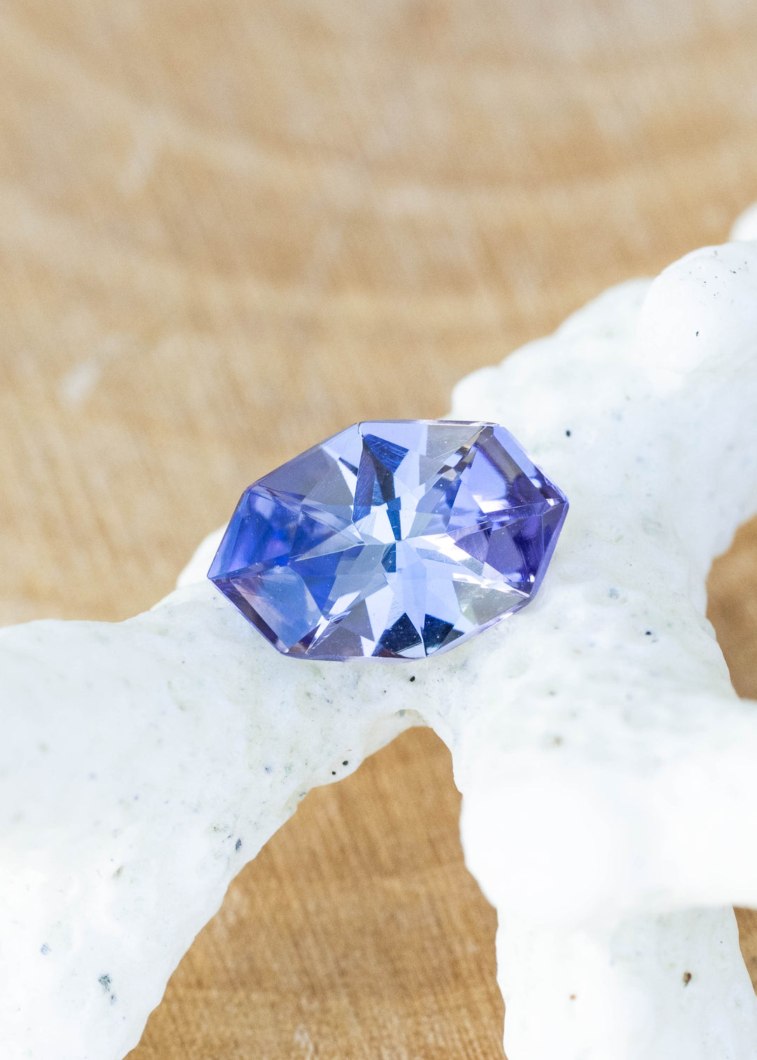 Natural 1.11 carat purple blue tanzanite from Merelani Hills, Tanzania featuring a custom geometric marquise cut with shifting violet, teal, and gray tones displayed on coral.