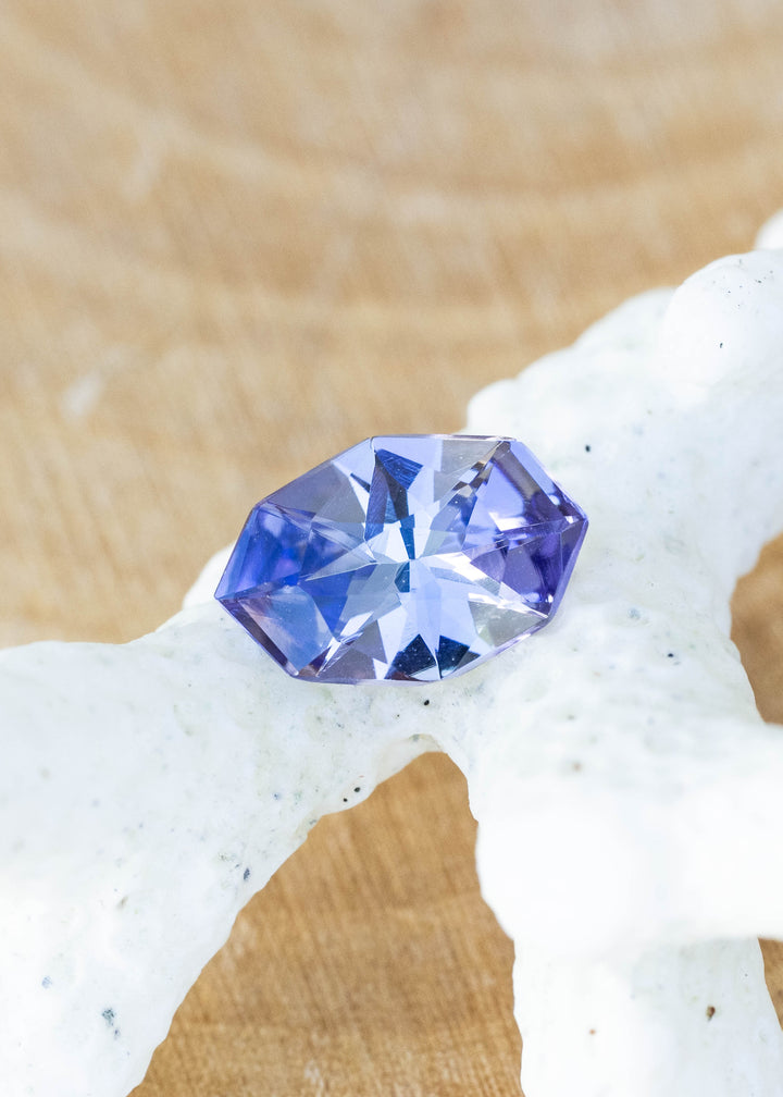 Natural 1.11 carat purple blue tanzanite from Merelani Hills, Tanzania featuring a custom geometric marquise cut with shifting violet, teal, and gray tones displayed on coral.