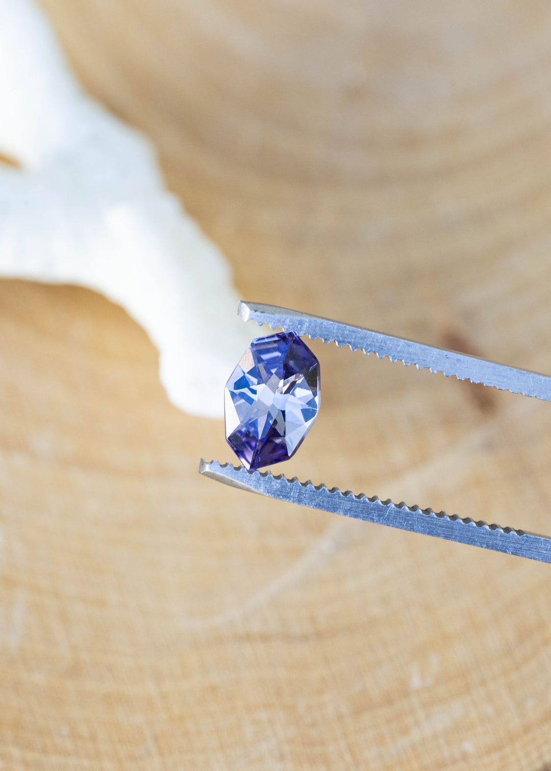 Close-up of a natural 1.11 carat Merelani Hills tanzanite in tweezers showcasing its precision custom geometric marquise cut and pleochroic purple, teal, and gray color.