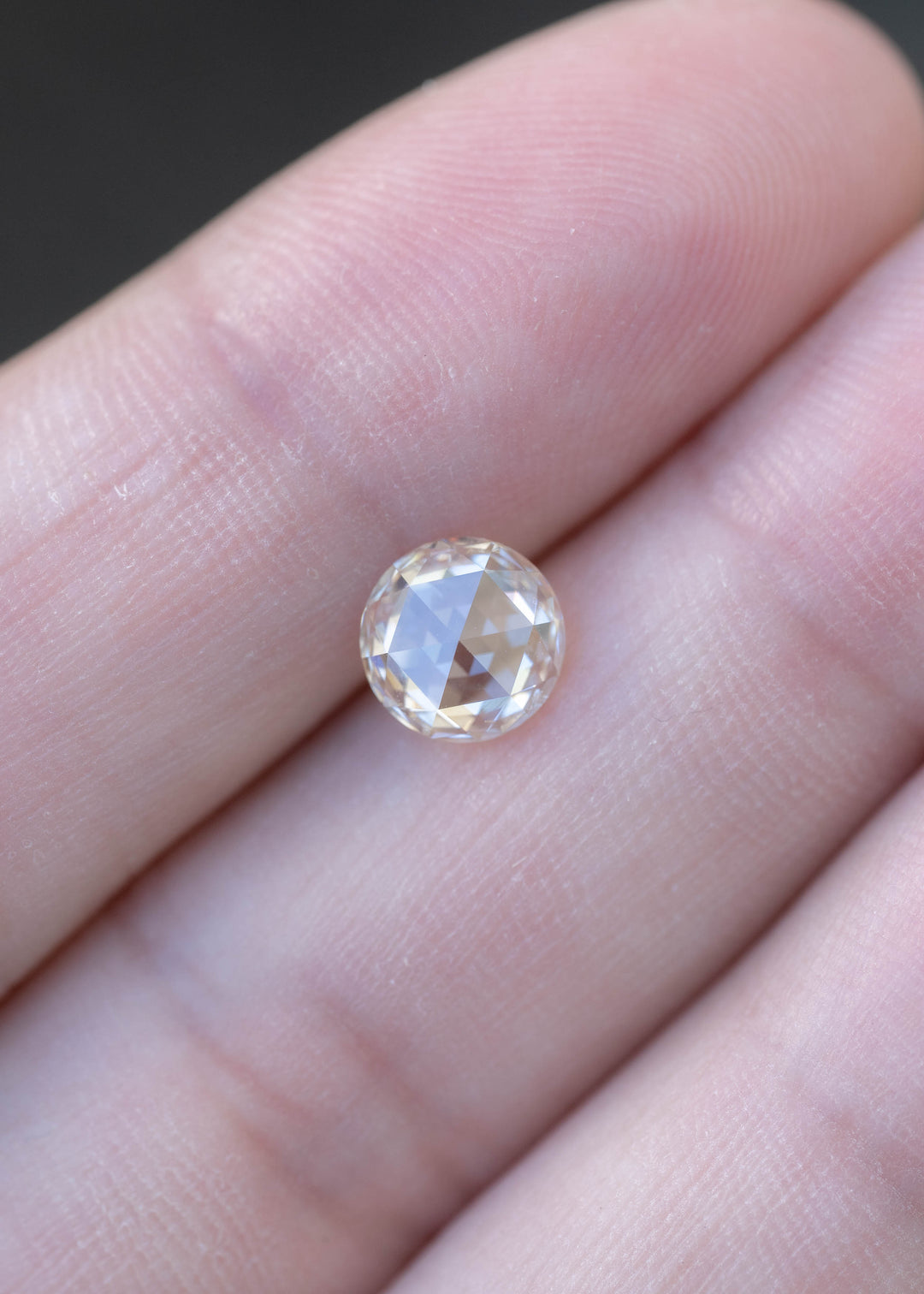 Natural 1.14 carat blush champagne rose cut diamond resting on fingertips for size comparison, displaying warm pastel tones and classic rose-cut faceting