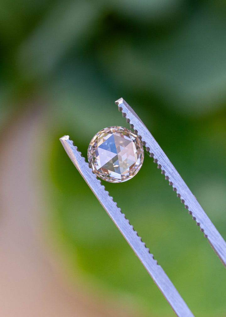 Front-facing view of a natural 1.14 carat blush champagne rose cut diamond held in gem tweezers, showcasing its symmetrical round shape and antique faceting.