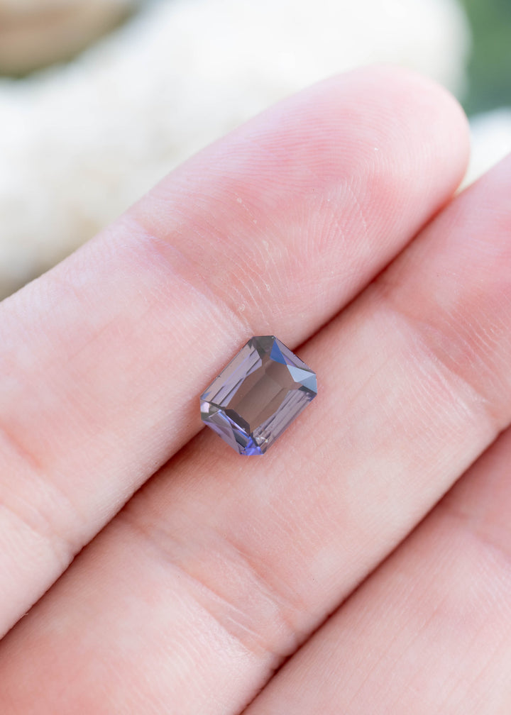 Natural 1.19 carat custom portrait-cut tanzanite displayed on fingertips, highlighting its elegant proportions and shifting green, violet, and silvery tones.