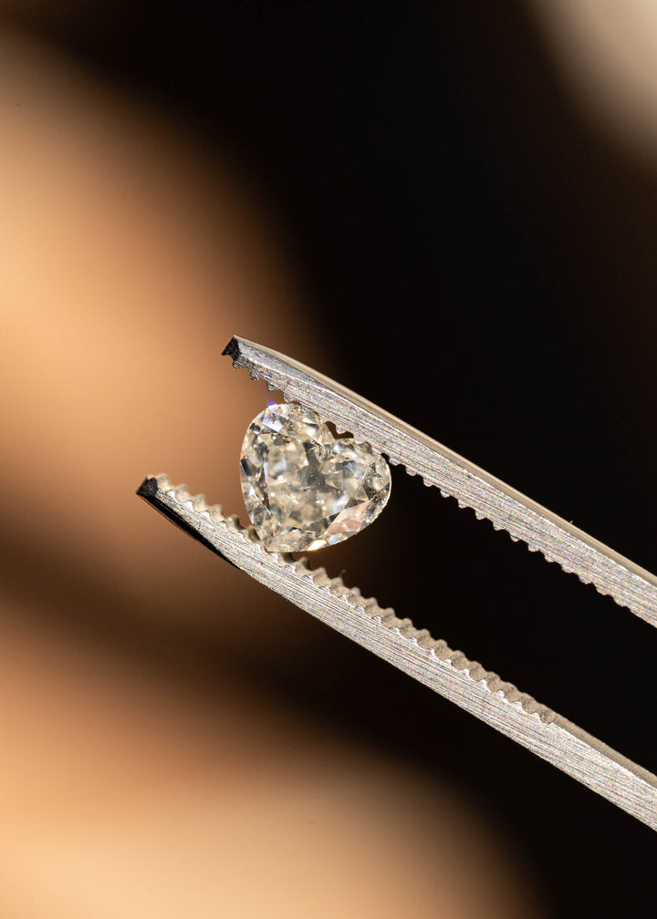 Close-up of a natural antique style heart cut salt and pepper diamond in tweezers, showing broad flashes of brilliance, natural inclusions, and balanced heart proportions.