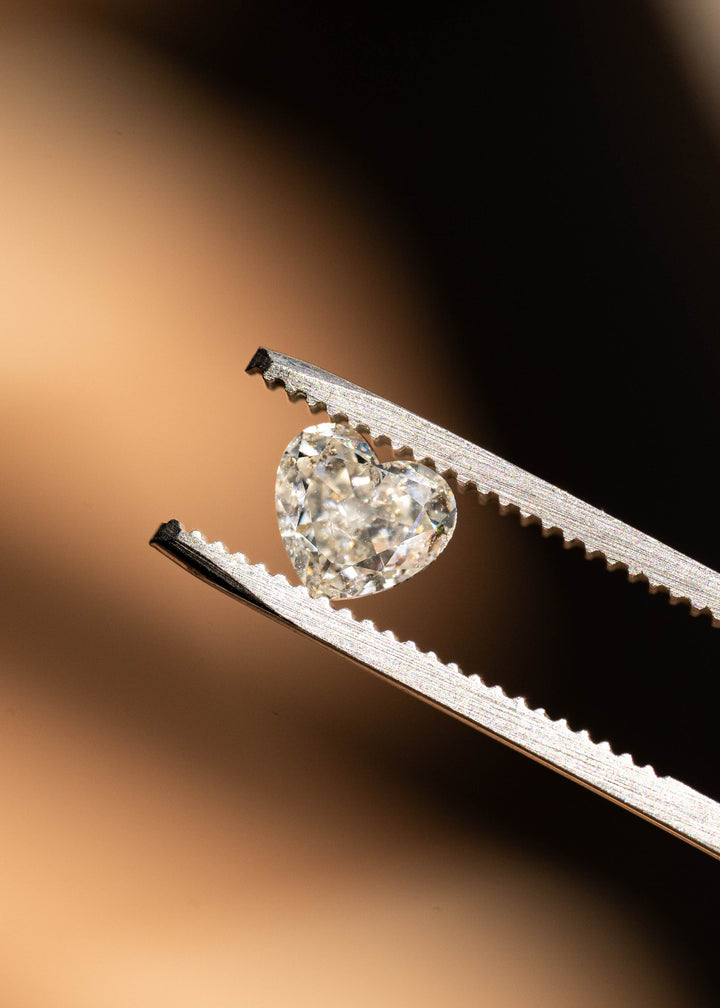 Angled close-up of a natural salt and pepper heart cut diamond in tweezers, displaying vintage-inspired faceting, internal crystal inclusions, and bright white reflections.