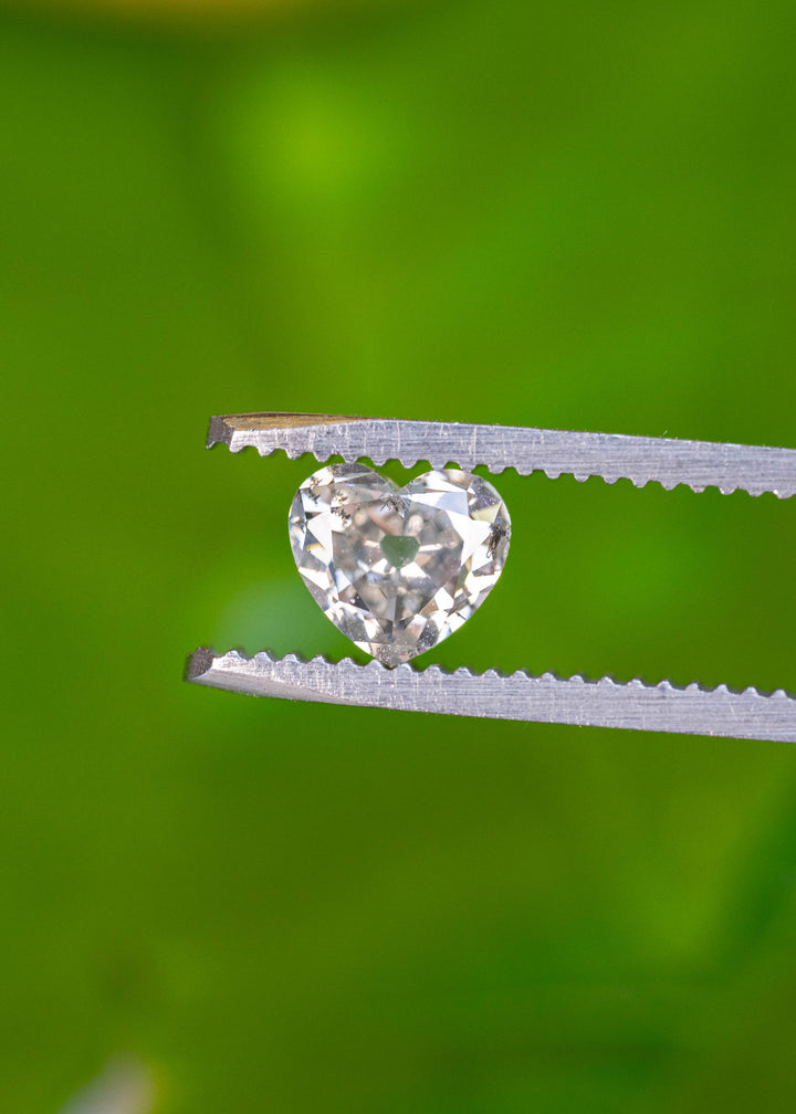 Front-facing view of a natural 1.21 carat antique style heart cut salt and pepper diamond held securely in gem tweezers, highlighting its symmetrical heart shape and natural inclusions.