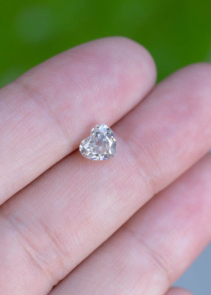 Natural 1.21 carat antique style heart cut salt and pepper diamond displayed on fingertips for size comparison, revealing its unique internal characteristics and elegant heart outline.
