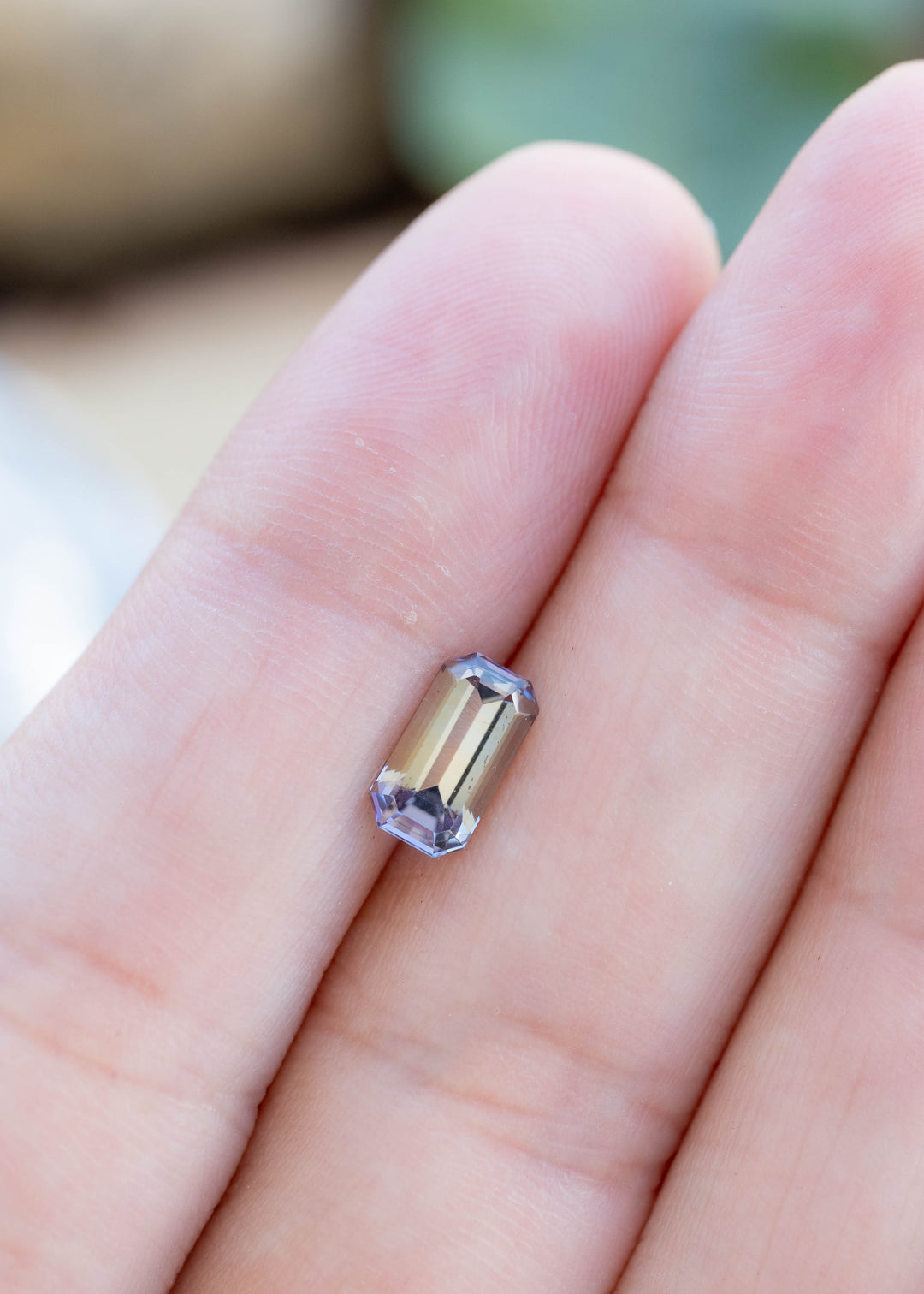 Natural 1.22 carat emerald-cut tanzanite displayed on fingertips, showing its elongated proportions and delicate periwinkle purple hue.