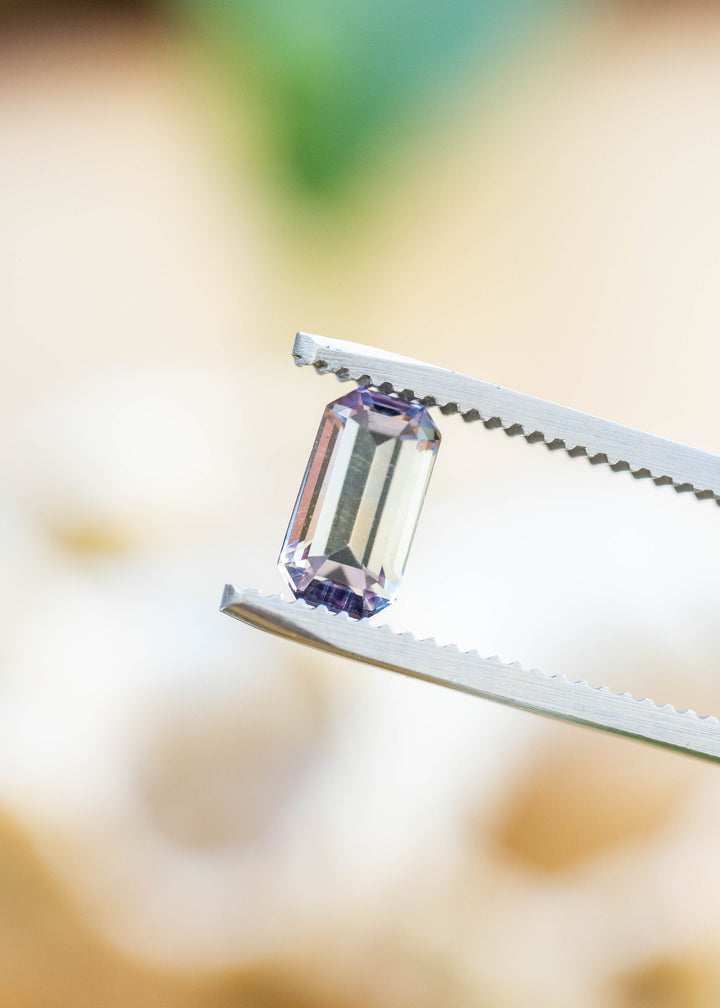 Close-up of a natural 1.22 carat untreated Merelani Hills tanzanite in tweezers highlighting its emerald cut and soft periwinkle purple color.