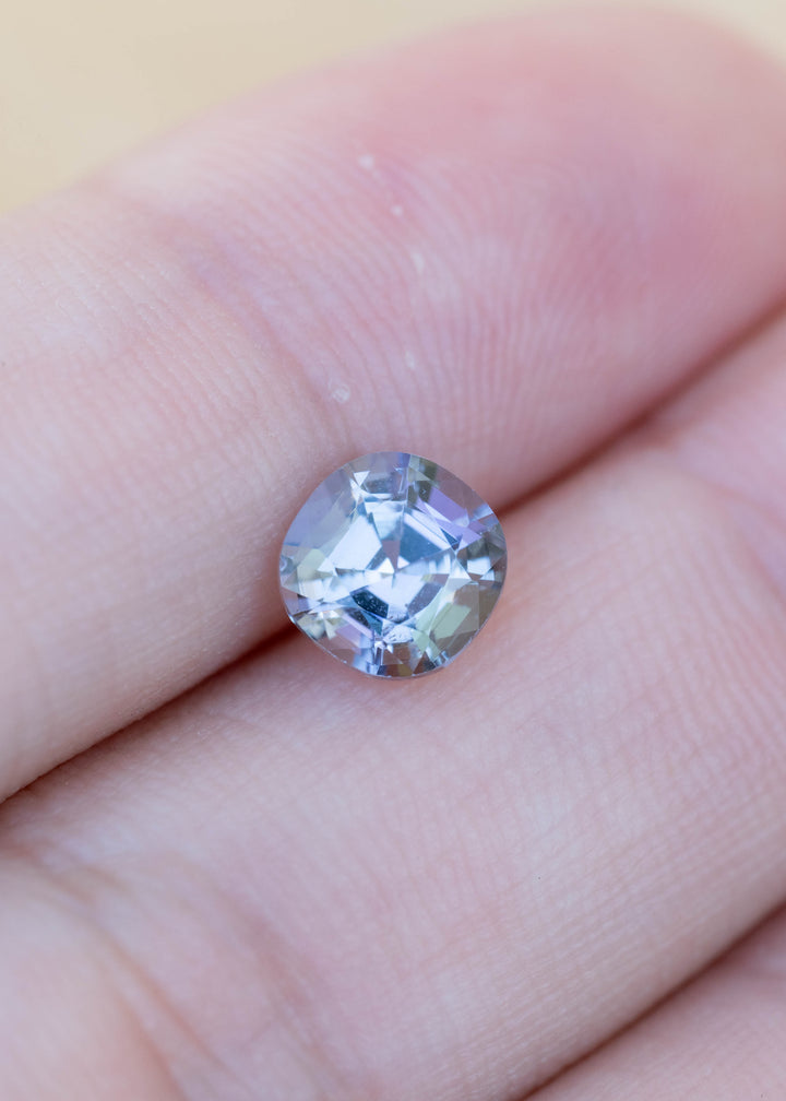 Natural 1.32 carat modified cushion tanzanite displayed on fingertips, revealing its elegant proportions and shifting blue, green, teal, and purple coloration.