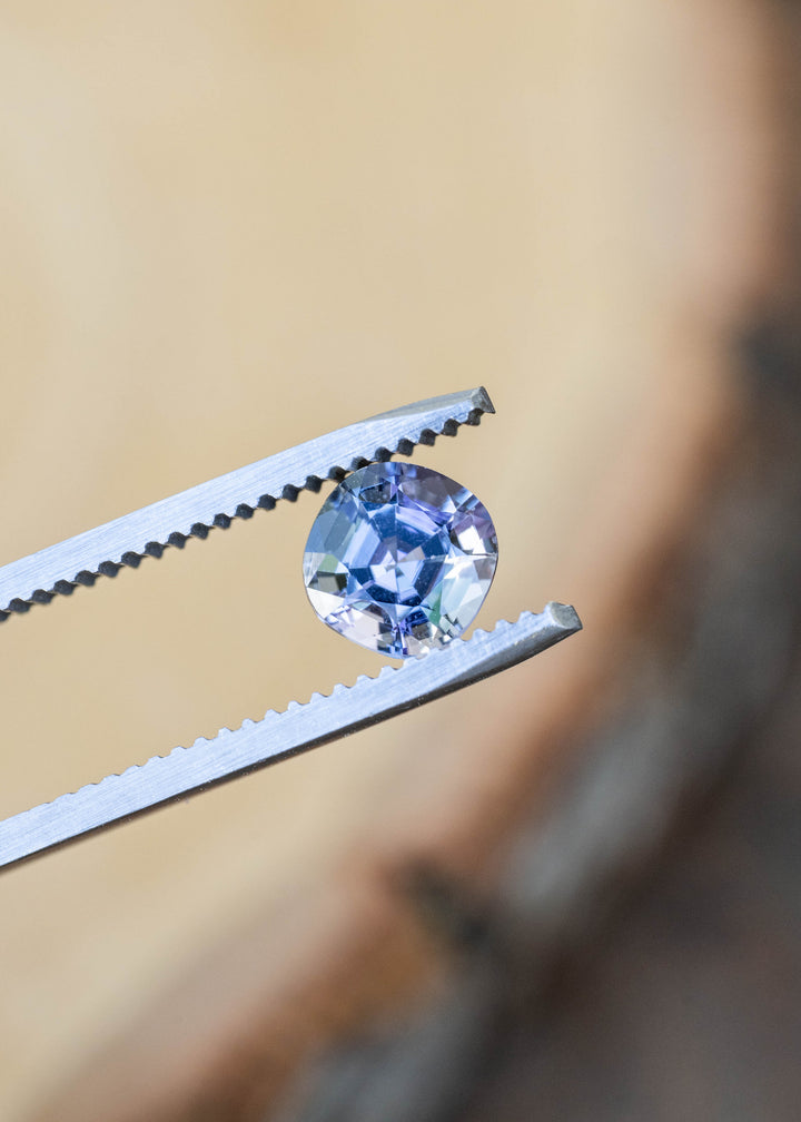 Close-up of a natural 1.32 carat untreated Merelani Hills tanzanite in tweezers highlighting its modified cushion cut and vibrant pleochroic blue, teal, green, and purple tones.
