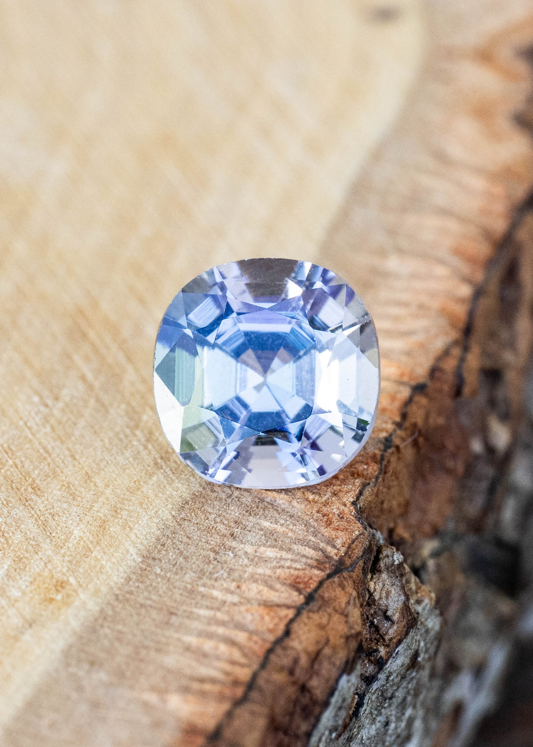 Natural 1.32 carat untreated tanzanite from Merelani Hills, Tanzania displayed on natural wood, showcasing its modified cushion cut and shifting blue, teal, green, and purple colors.