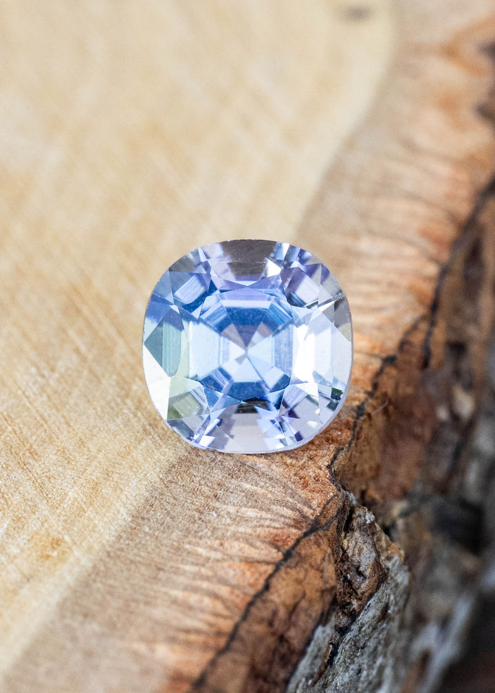 Natural 1.32 carat untreated tanzanite from Merelani Hills, Tanzania displayed on natural wood, showcasing its modified cushion cut and shifting blue, teal, green, and purple colors.