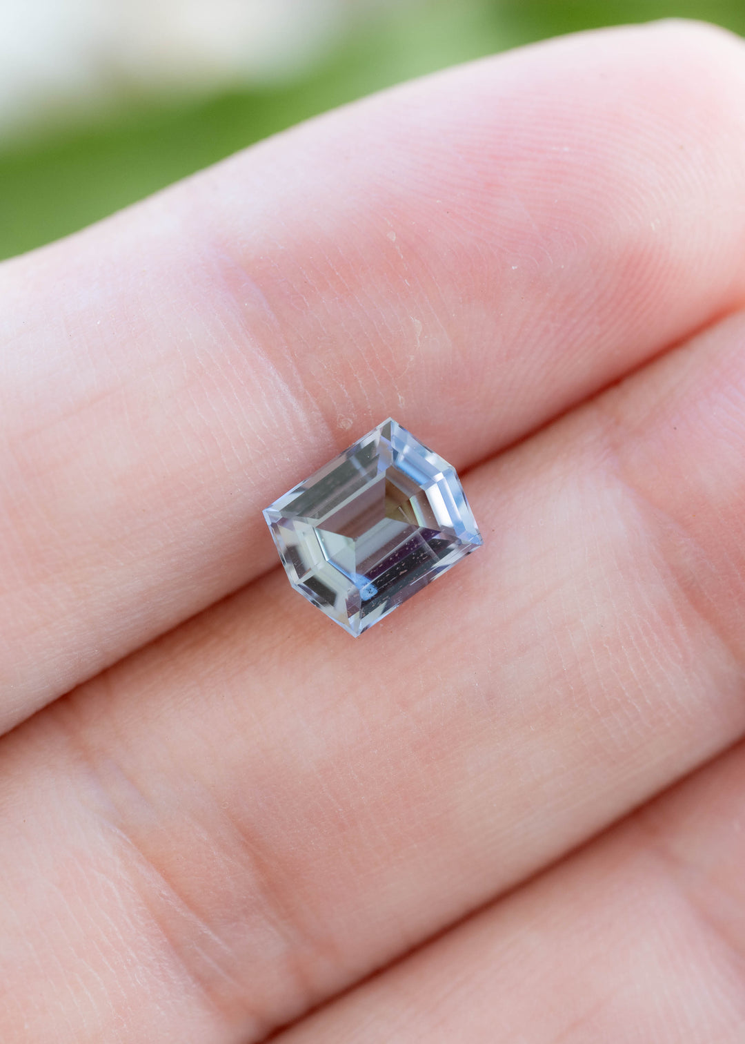 Natural 1.53 carat geometric step cut tanzanite shown on fingertips, revealing its elegant proportions and pleochroic blue, green, and violet colors.