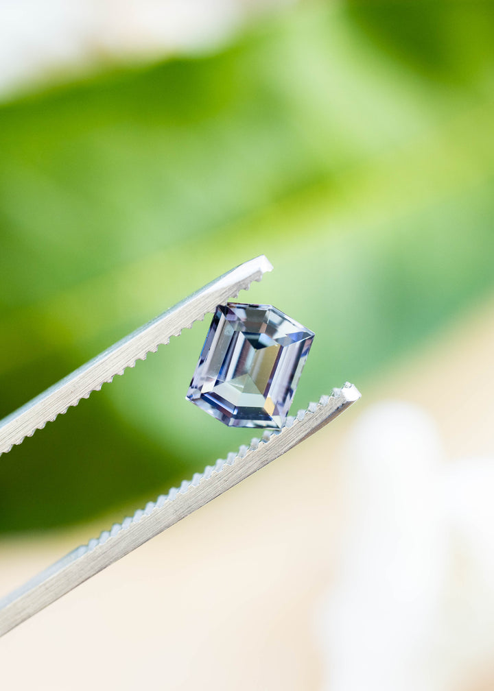 Close-up of a natural 1.53 carat untreated tanzanite in tweezers highlighting its custom hexagonal step cut and shifting mermaid blue, green, and purple hues.