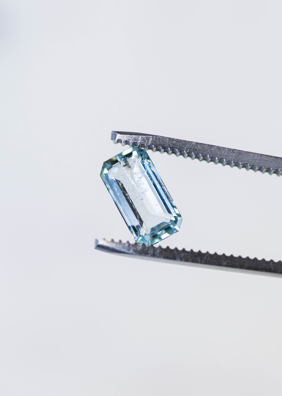 Close-up of an untreated Colorado aquamarine held in tweezers, showcasing its custom octagonal step cut, transparent crystal, and light medium blue hue.
