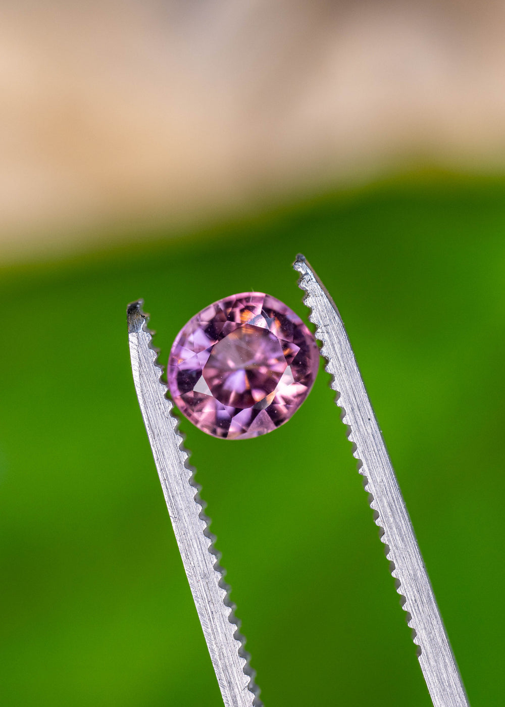 Close-up of an untreated Congolese pink tourmaline in tweezers showcasing an antique custom radiant round cut and vivid pink sparkle.