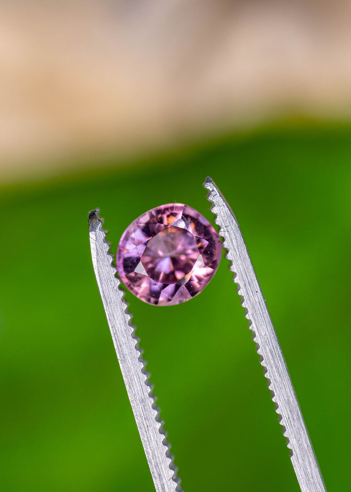 Close-up of an untreated Congolese pink tourmaline in tweezers showcasing an antique custom radiant round cut and vivid pink sparkle.