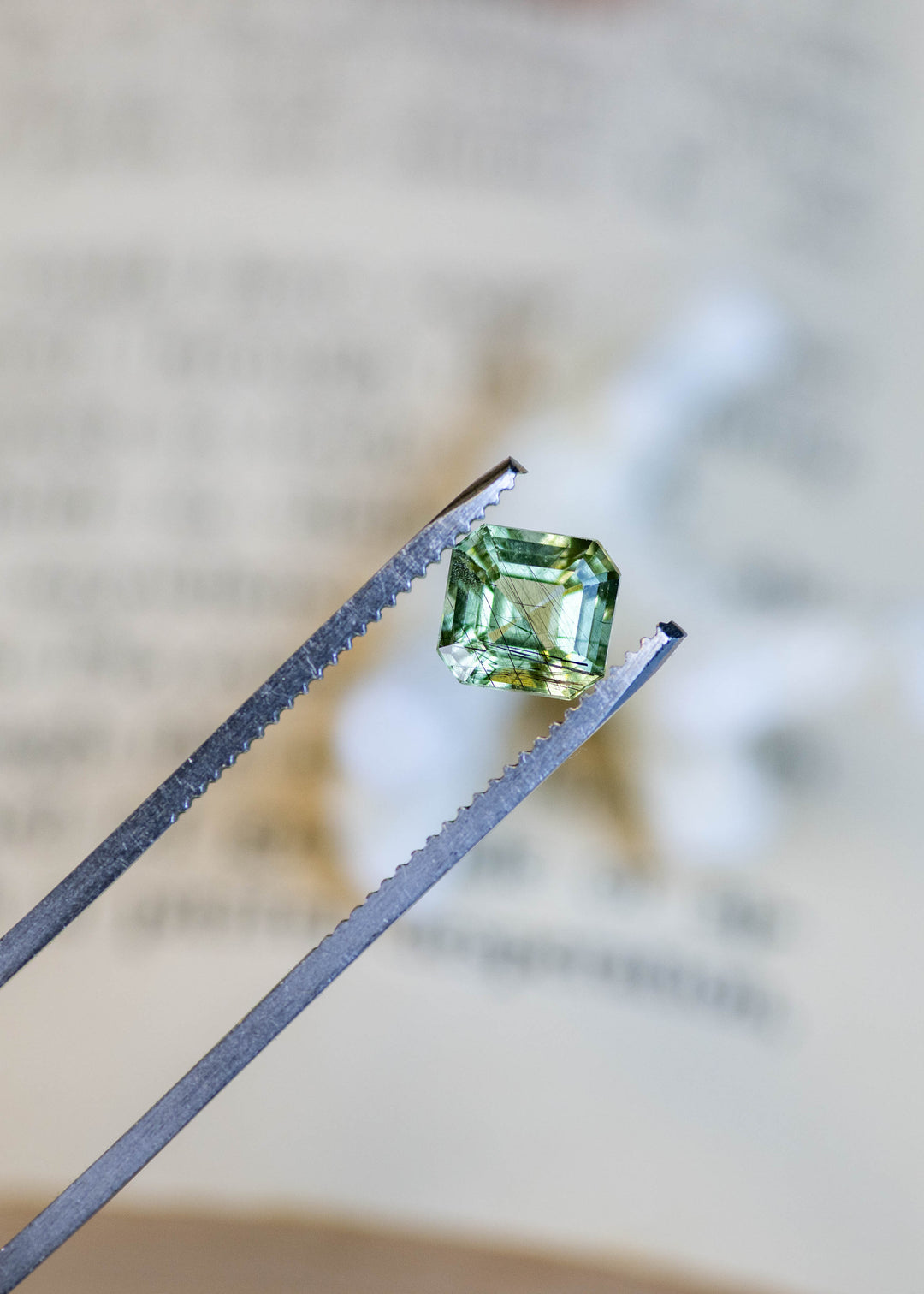 Close-up of a natural untreated Pakistani peridot held in tweezers, highlighting its custom Asscher cut, lime-green color, and distinctive natural needle inclusions.