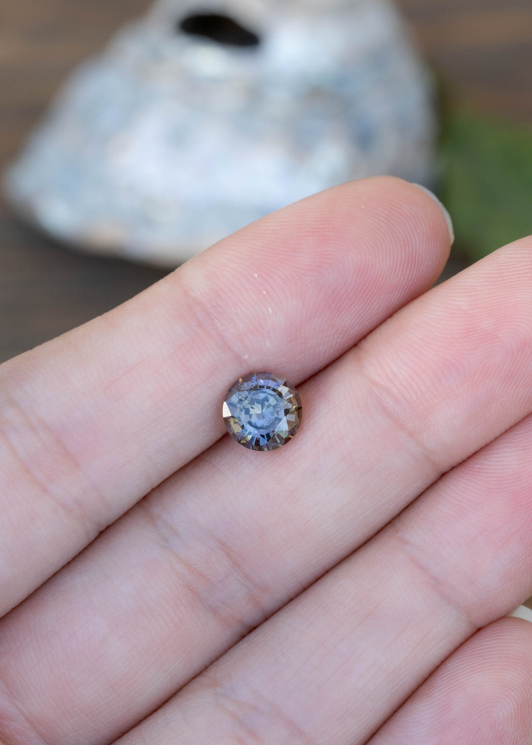 Natural 1.72 carat Merelani tanzanite shown on fingertips featuring a precision custom round mixed cut with vibrant parti coloration.