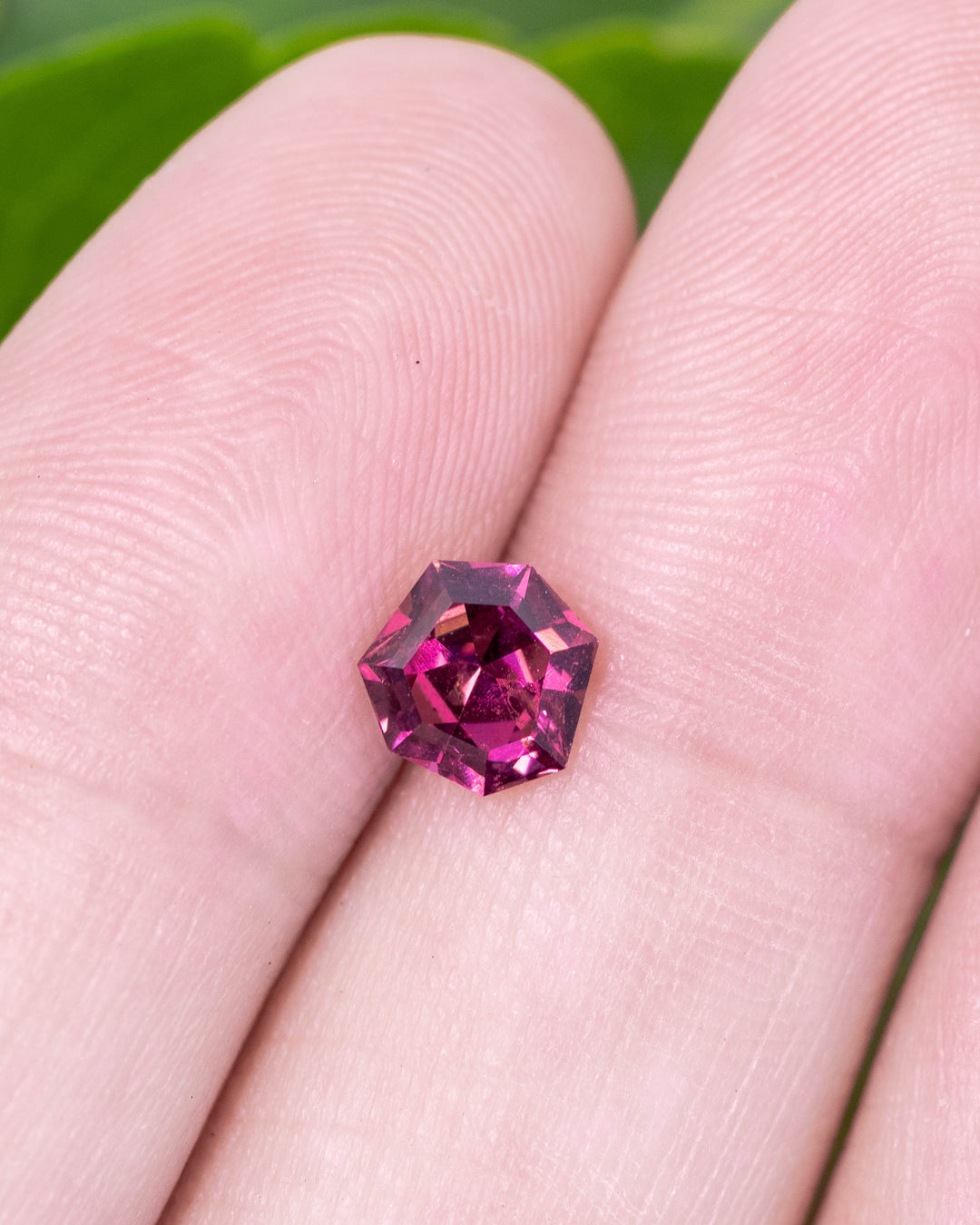 1.00 carat garnet displayed on fingertip, reflecting deep red and magenta tones through its geometric shield mixed cut design, untreated gemstone originating from Kenya.