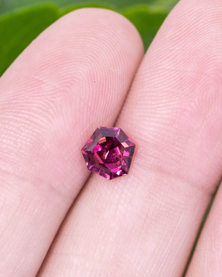 1.00 carat garnet displayed on fingertip, reflecting deep red and magenta tones through its geometric shield mixed cut design, untreated gemstone originating from Kenya.