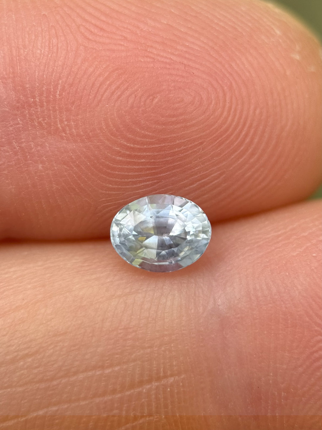 Custom oval cut sapphire from Montana held in tweezers showcasing its unheated pastel tones