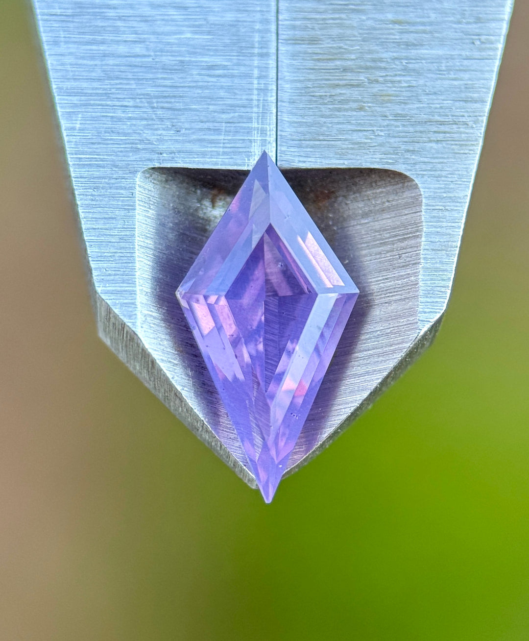 Precision kite cut pink and purple opalescent loose sapphire resting on the tip of calipers. Under natural light the purple hue shines. 