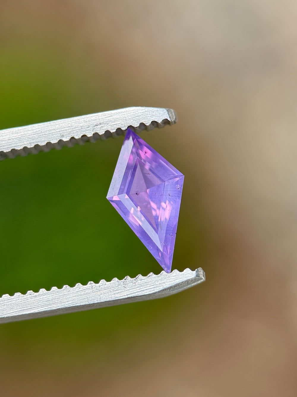 1.00 carat loose opalescent sapphire held in gem tweezers showing off precision faceting and vibrant pink and purple hues.