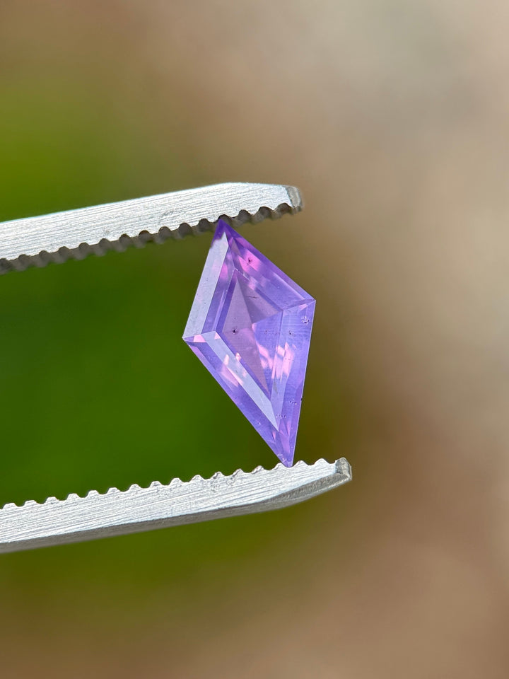 1.00 carat loose opalescent sapphire held in gem tweezers showing off precision faceting and vibrant pink and purple hues.