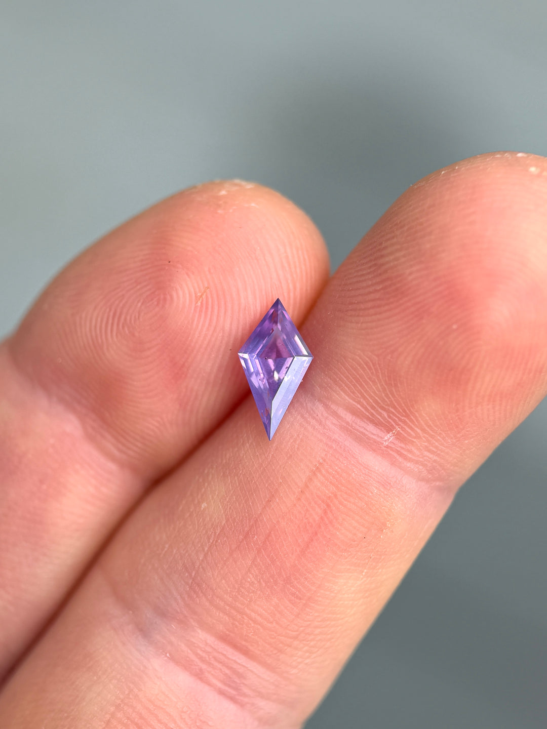 Faceted purple loose sapphire from Madagascar held between fingers against a neutral background