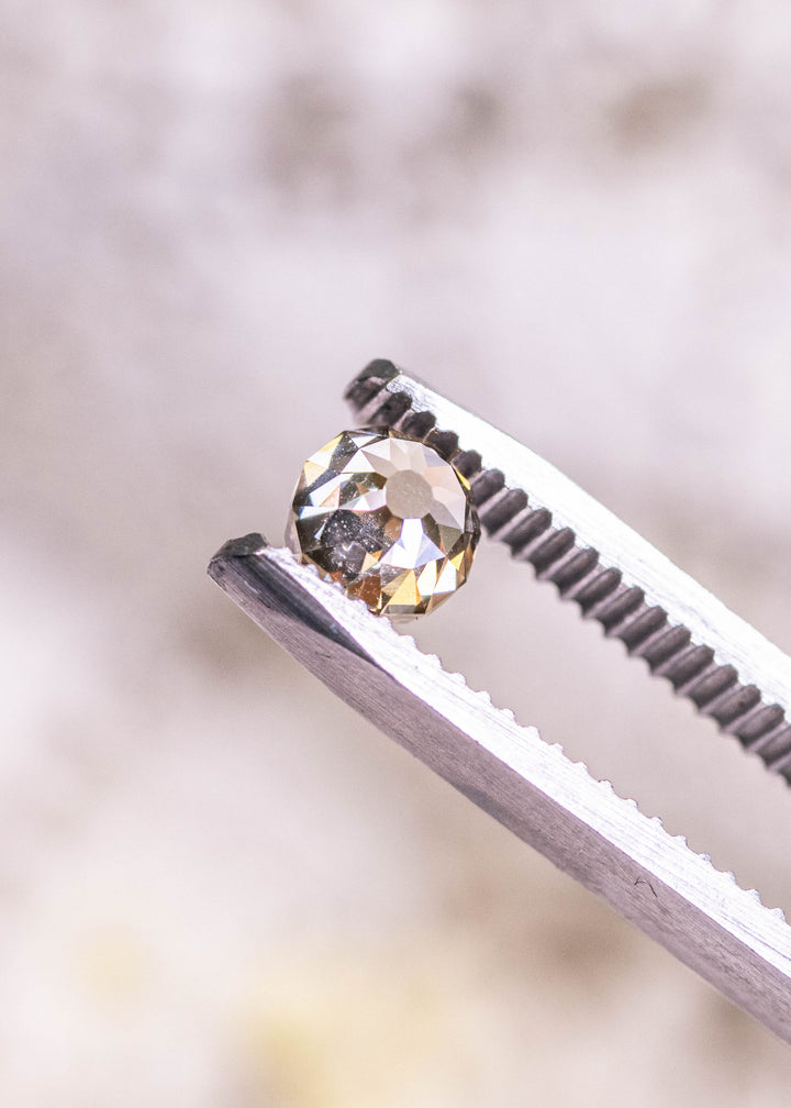 Loose rosy champagne fancy brown Mughal cut diamond held in tweezers, highlighting its domed crown, symmetrical facets, and soft champagne glow.