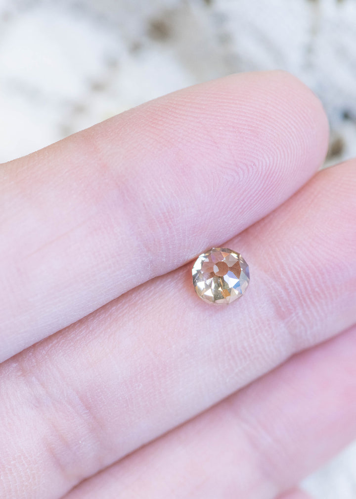 Loose rosy champagne fancy brown Mughal cut diamond resting on fingertips, illustrating its size, VVS1 clarity, and warm natural color.