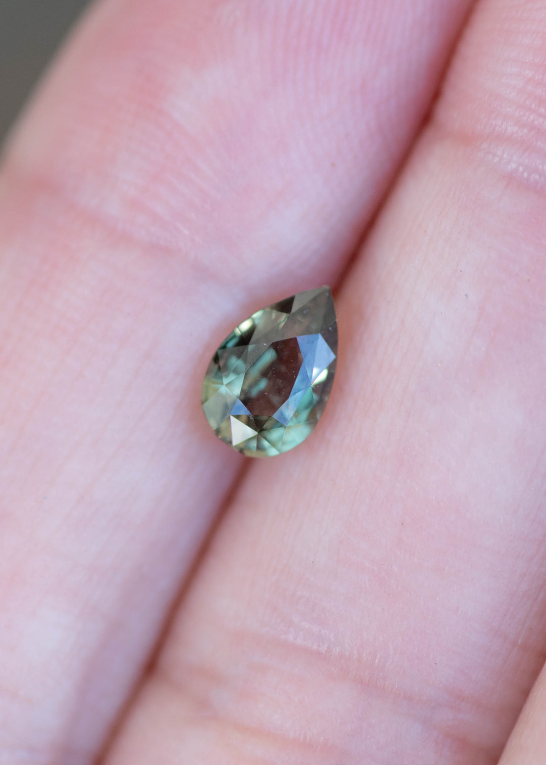 Pear cut alexandrite gemstone held between two fingers on a light skin background