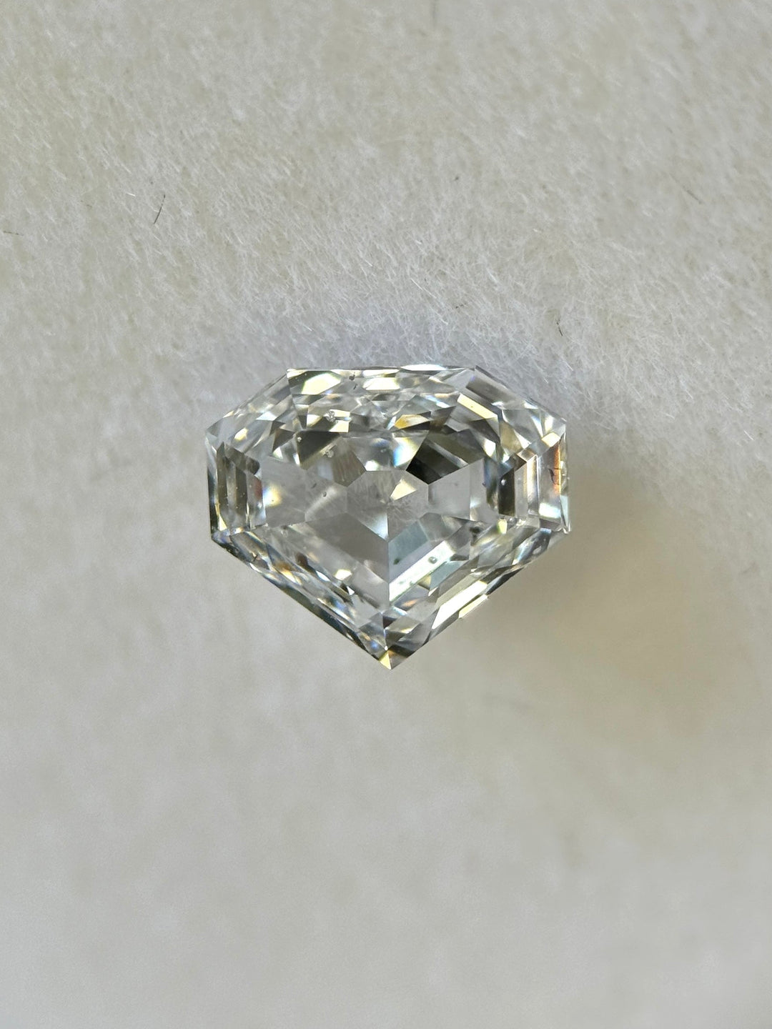 Close-up of a 1.01 carat E color SI1 clarity shield step cut diamond from Gahcho Kué, Canada, resting on a white surface. The natural untreated diamond displays mirror-like precision and sharp geometric facets.