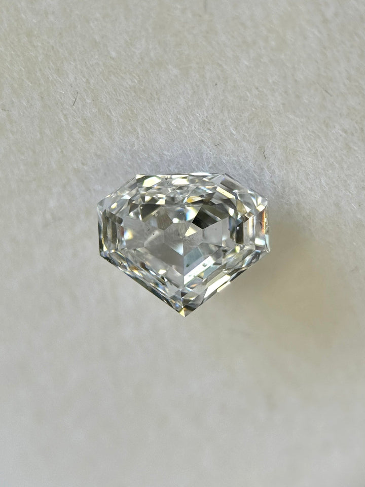 Close-up of a 1.01 carat E color SI1 clarity shield step cut diamond from Gahcho Kué, Canada, resting on a white surface. The natural untreated diamond displays mirror-like precision and sharp geometric facets.