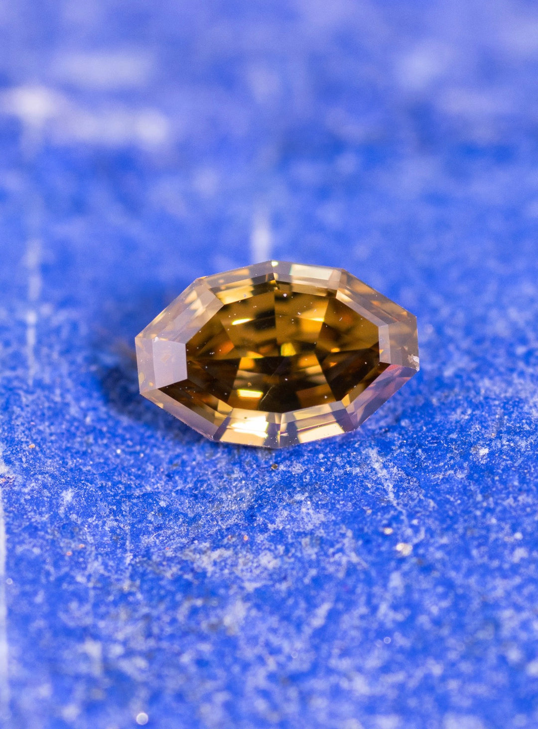 Loose fancy orangish yellow brown diamond resting on natural blue stone showing the antique style moval step cut and warm golden amber color.