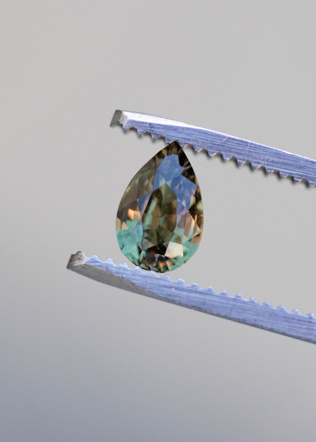 Color changing alexandrite gemstone shifting from green to red under natural lighting held in tweezers.