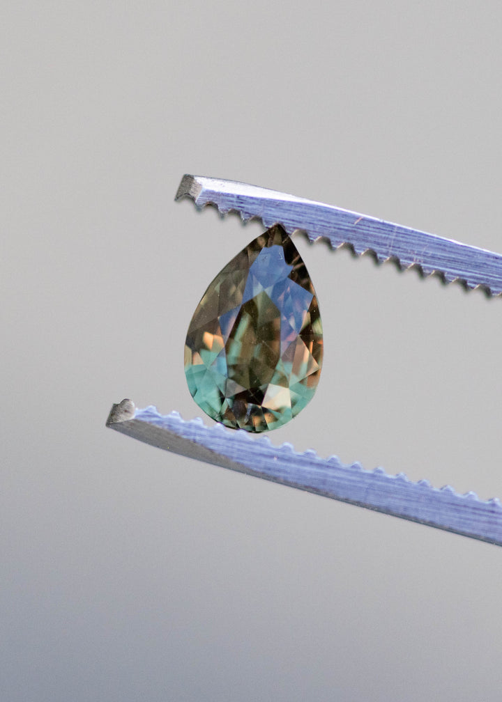 Color changing alexandrite gemstone shifting from green to red under natural lighting held in tweezers.