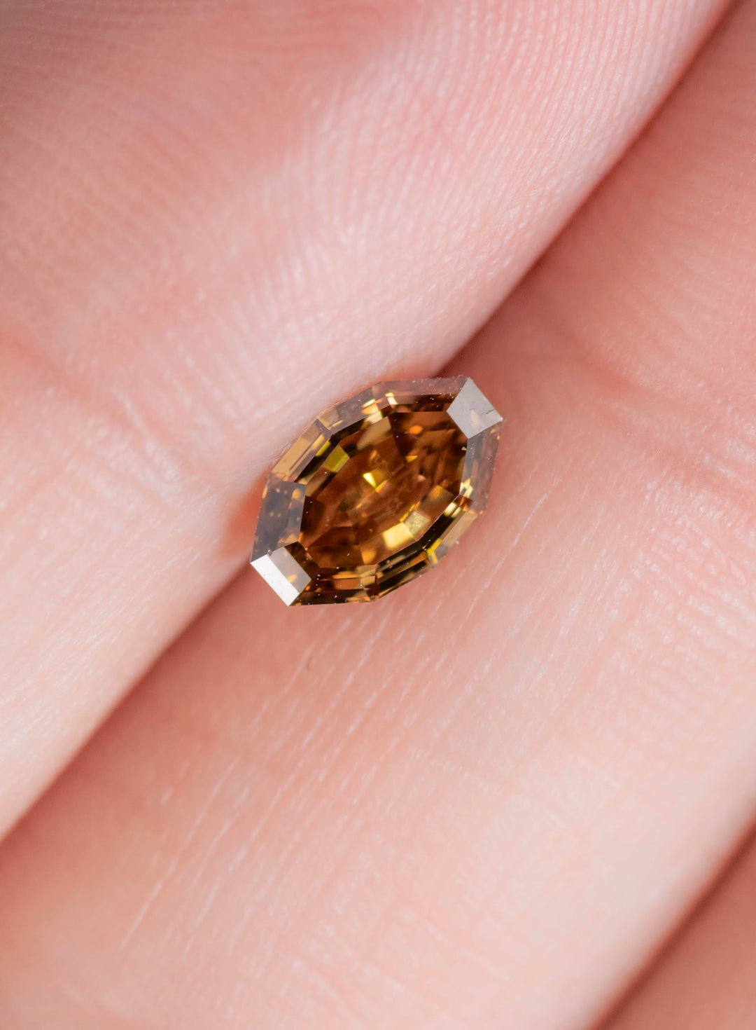 Fancy orangish yellow brown diamond shown on a fingertip highlighting the antique moval step cut and natural warm brown yellow tone.