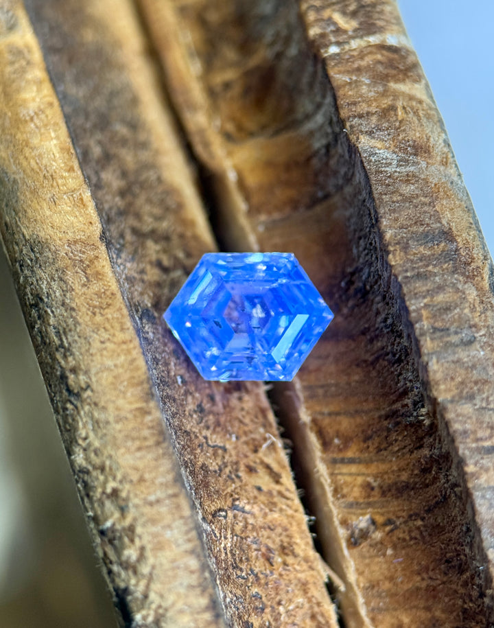 1.01 carat G color I2 clarity diamond from Gahcho Kué, Canada, photographed on textured wood with a hexagonal step cut design. A UV light highlights the diamond’s blue fluorescence and internal structure.