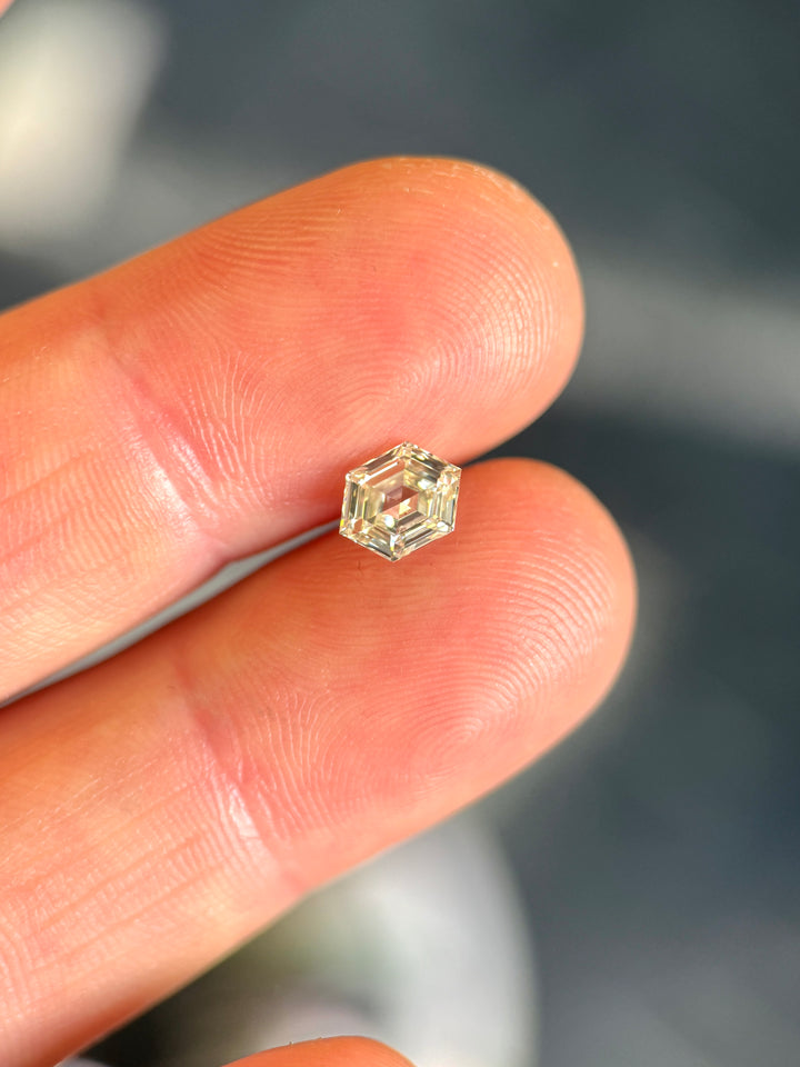 1.01 carat O–P color VVS2 clarity diamond from Gahcho Kué, Canada, balanced on a fingertip to show its scale and precision. The hexagonal step cut reveals clean lines and geometric brilliance.