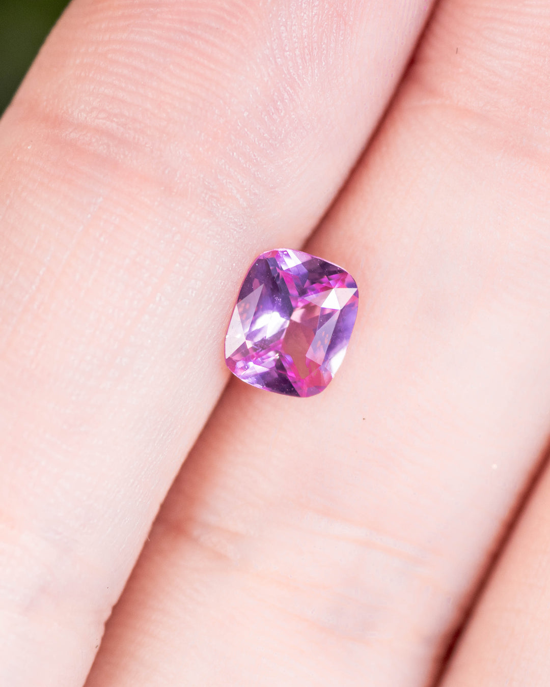 1.01 carat pink sapphire displayed on fingertip, capturing sparkle and clarity of its cushion brilliant cut under natural light, untreated sapphire from Madagascar.