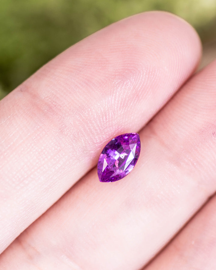 1.01CT purple pink sapphire resting on fingertip, capturing the sparkle and precision of its marquise brilliant cut under natural light, untreated gemstone from Sakaraha, Madagascar.