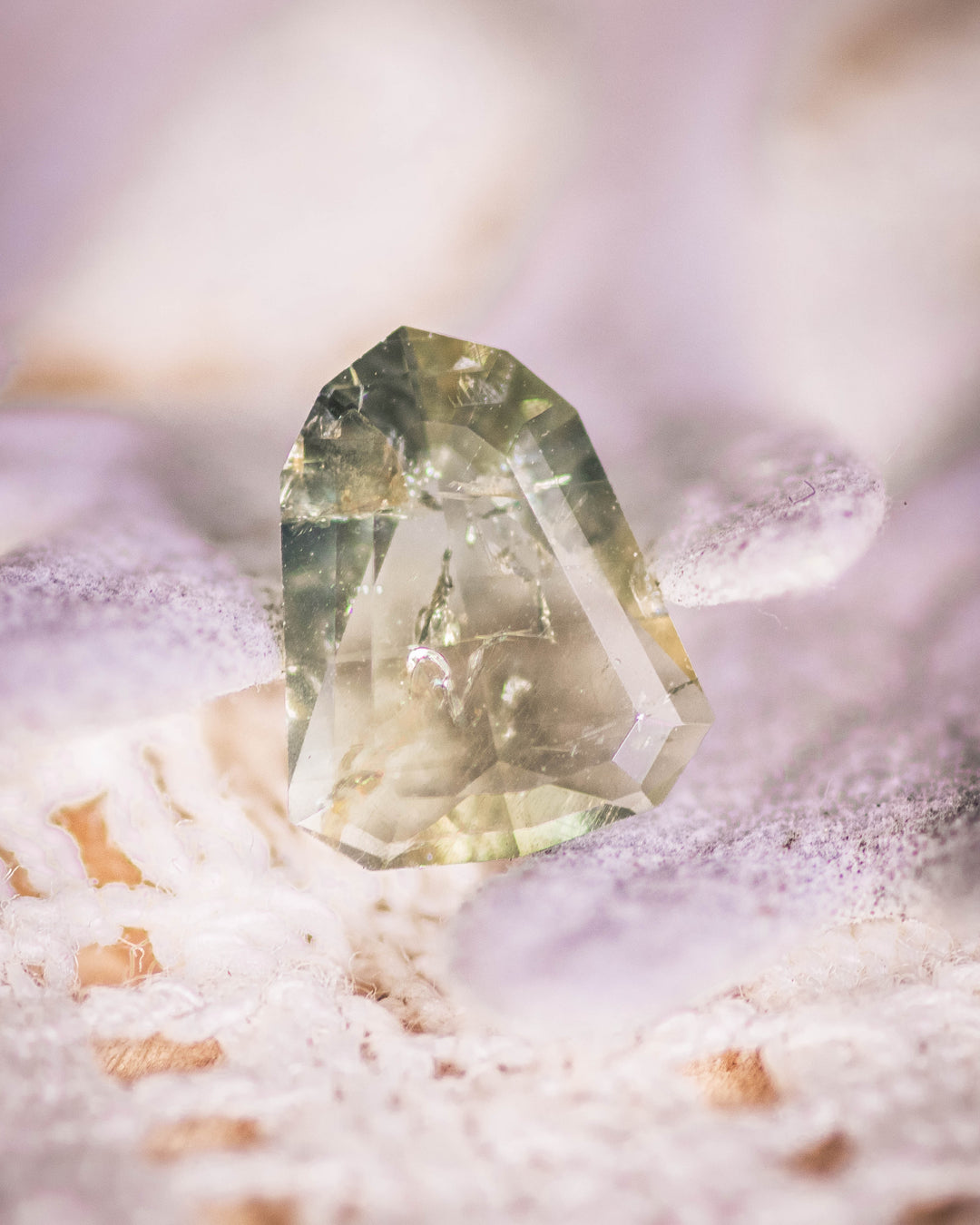 1.01 carat yellow teal and green sapphire resting on soft lavender textile background, showing transparency and step facets of its custom shield portrait cut, untreated gem from Umba River, Tanzania.