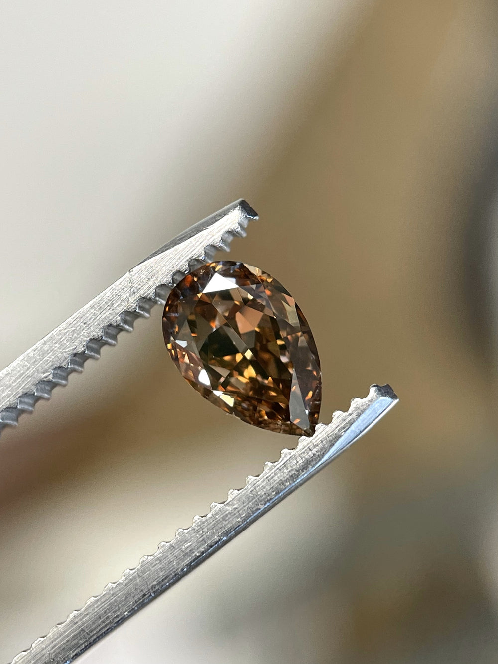 Close-up of a 1.01-carat Fancy Dark Orangy Brown diamond held in tweezers, showcasing its pear modified brilliant cut and intense color.