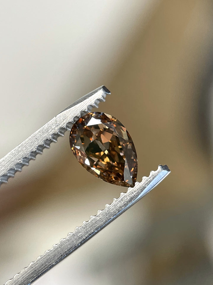 Close-up of a 1.01-carat Fancy Dark Orangy Brown diamond held in tweezers, showcasing its pear modified brilliant cut and intense color.