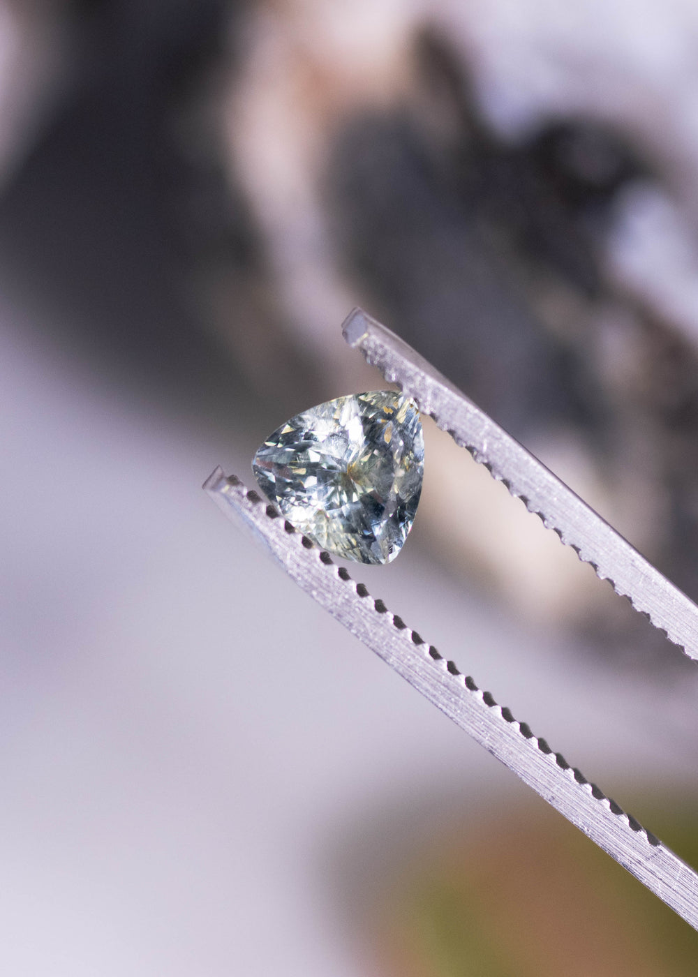 1.01 carat green yellow gray Montana sapphire trillion cut held in jeweler tweezers showing sharp triangular symmetry and light return