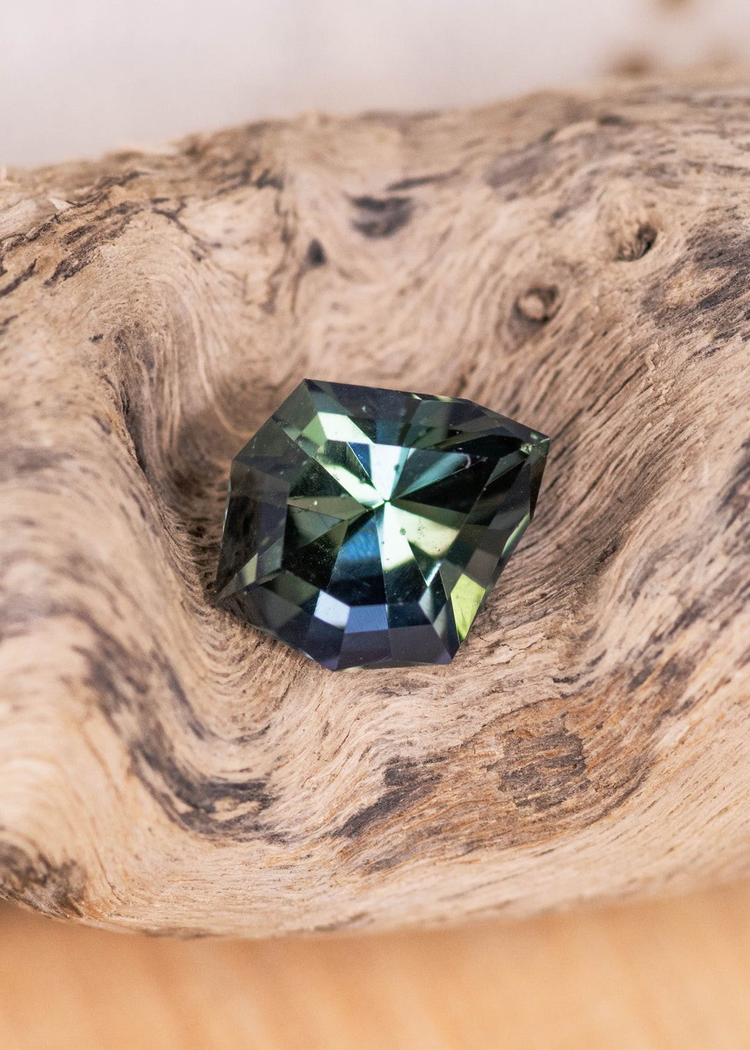 Loose teal blue green tanzanite resting on natural wood showing the custom geometric shield cut and color shifting facets from Merelani Hills Tanzania.