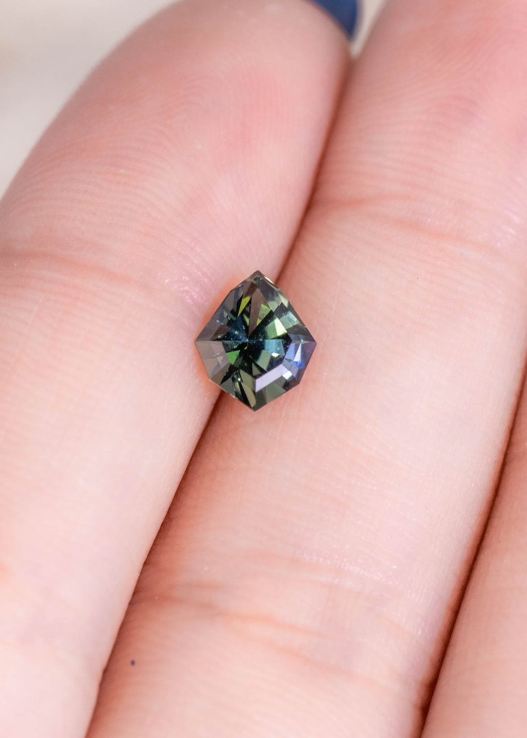 Loose teal green tanzanite shown on fingertips highlighting the geometric shield cut and the natural color mix of blue green tones.