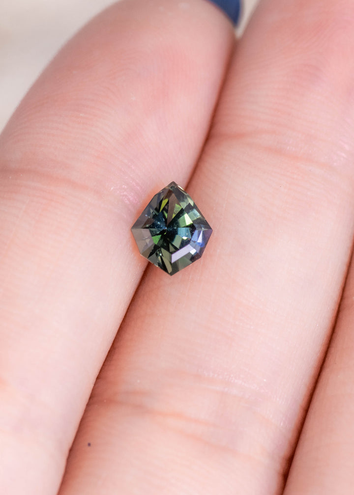 Loose teal green tanzanite shown on fingertips highlighting the geometric shield cut and the natural color mix of blue green tones.